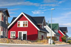 A row of vibrant, modern residential houses with red and grey siding under a blue sky, representing affordable housing options.