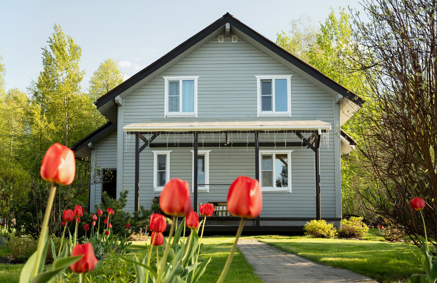 Front view of a two-story light green single-family home with red tulips in the foreground.