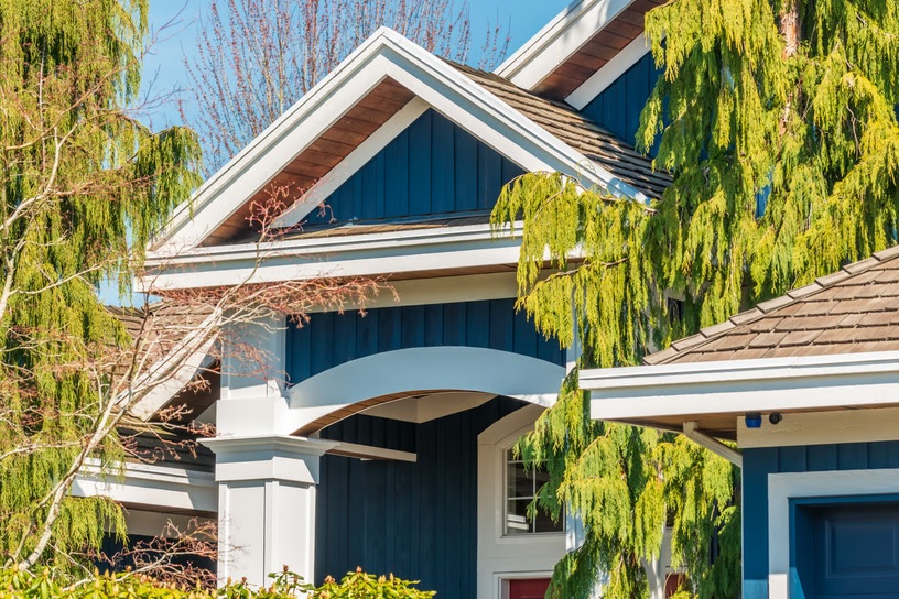 Close-up of a modern blue suburban home roofline surrounded by trees
